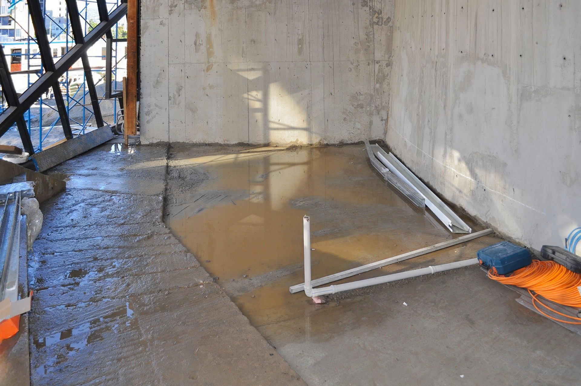 Water reflects daylight on the concrete floor of an active construction site in the interior.